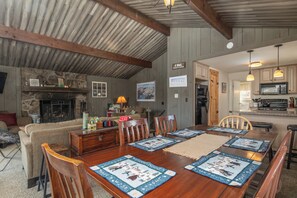 A cozy dining area with a wooden table, chairs, and a fireplace. There is a kitchen area with cabinets and a microwave. - Rustic cabin w/ mountain view & fireplace (Ludlow)