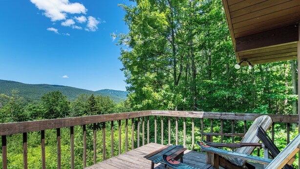 A wooden deck with a bench and a table, overlooking a forested area with hills in the distance.