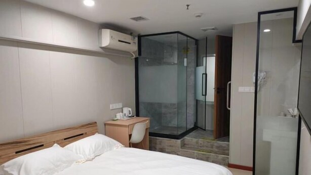 A hotel room with a bed, a desk, a glass-enclosed shower, and a wardrobe. - Sunshine Habitat Hotel (Dalian University of Technology) (Dalian)