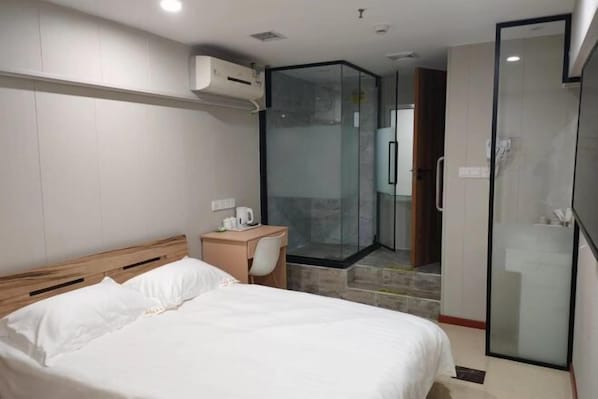 A hotel room with a bed, a desk, a shower area, and a glass-enclosed walk-in closet.
