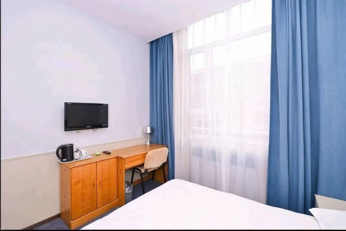 A hotel room with a bed, a desk with a chair, a television, and a window with curtains.
