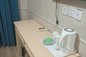 A hotel room with a wooden table, a remote control, a white electric kettle, a green electric heater, and a tray with a glass lid. - Sunshine Habitat Hotel (Dalian University of Technology) (Dalian)