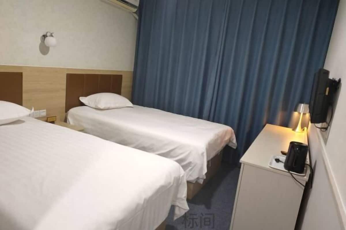 A hotel room with two single beds, a nightstand with a lamp, and a wall-mounted TV.