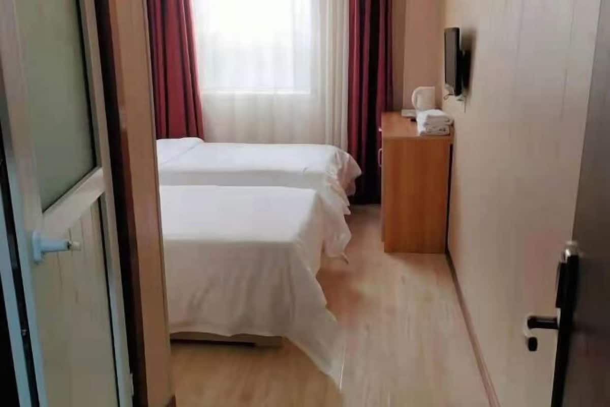 A hotel room with two beds, a wooden dresser, a television, and a window with curtains.