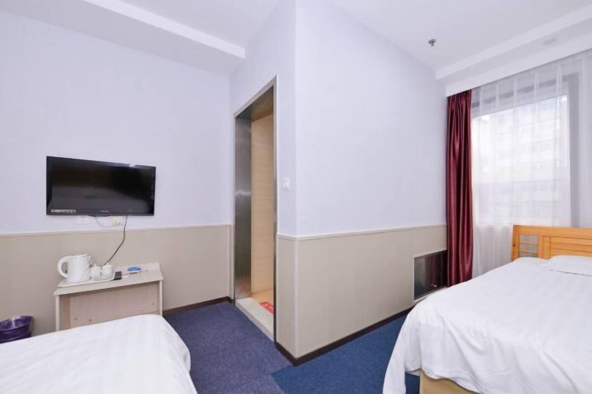 A hotel room with two beds, a TV, a small desk with a coffee maker, and a window with curtains.