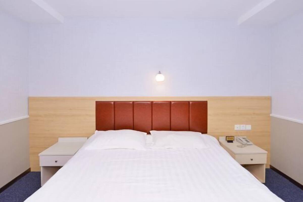 A hotel room with a bed, two bedside tables, a nightstand, a wall-mounted light, and a power outlet.
