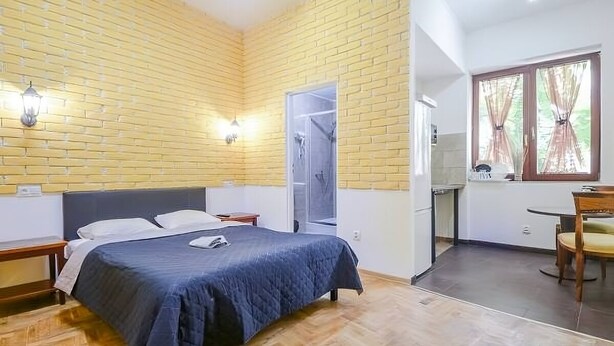 A bedroom with a bed, a nightstand, a wardrobe, a window with curtains, and a door leading to a bathroom. - Double apartment, Krakow Old Town (Kraków)