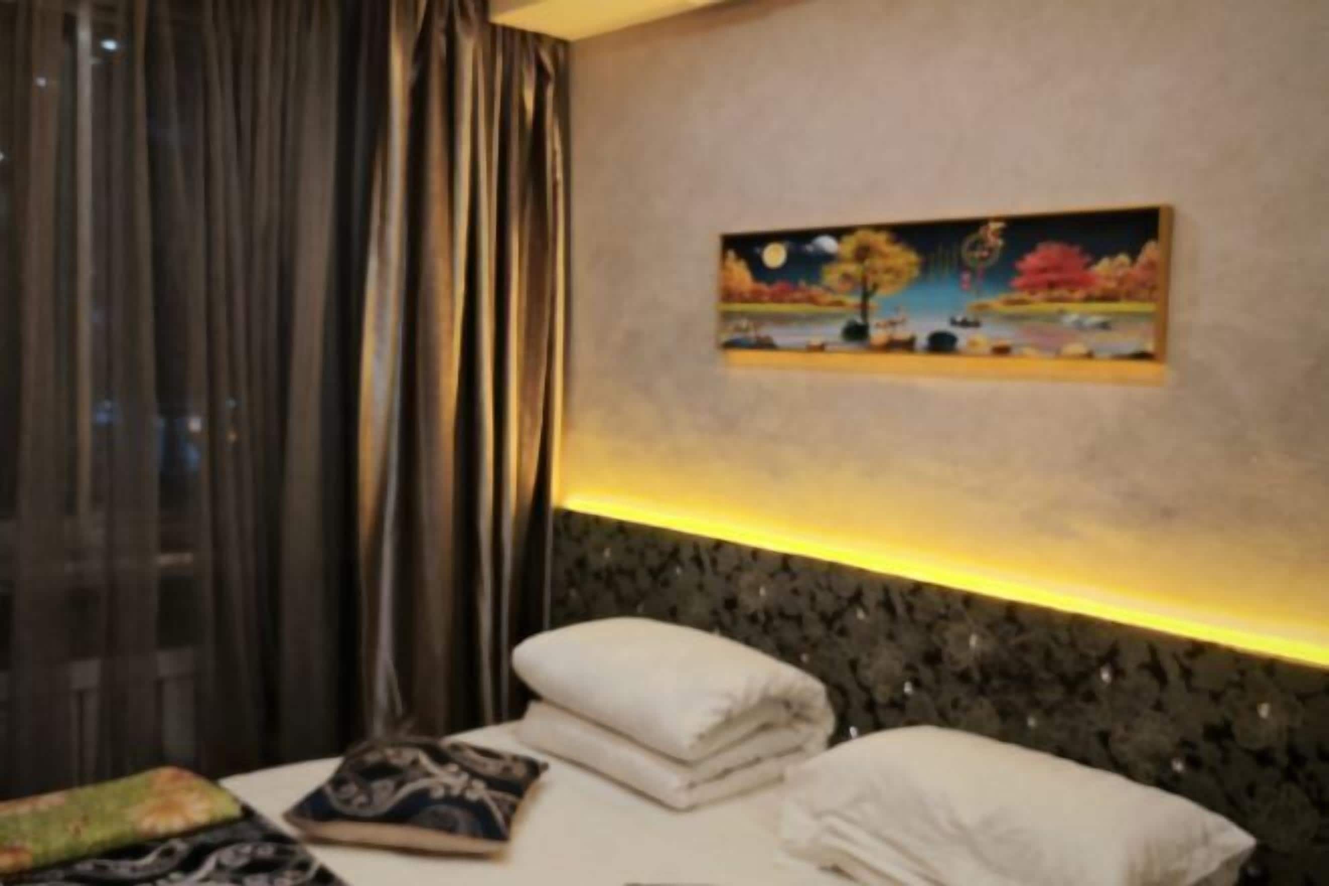 A hotel room with a bed, pillows, a painting on the wall, and a window with curtains.