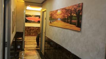 A hallway with a painting of a tree-lined path, a marble floor, and a door leading to another room.