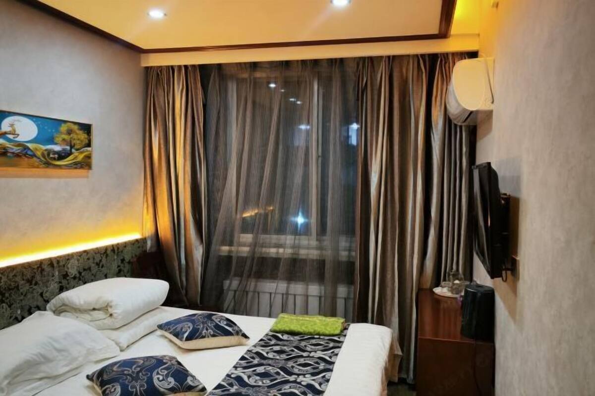 Una habitación de hotel con una cama, un cuadro en la pared, una ventana con cortinas y un televisor también en la pared.