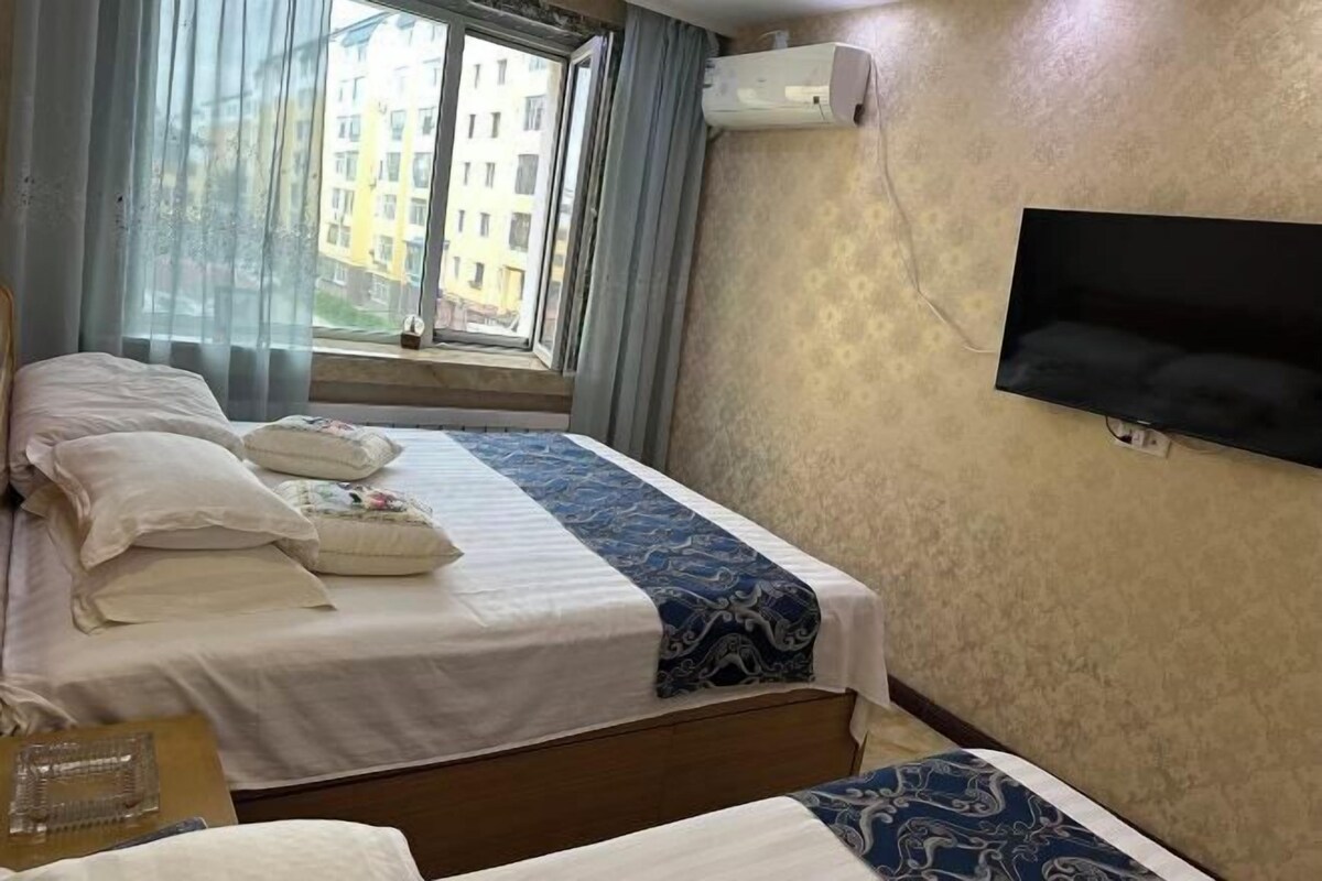 A hotel room with two beds, a TV mounted on the wall, and a window with curtains.