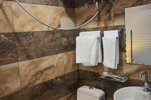 Kylpyhuone, jossa on marmorilaattoja, wc, pesuallas ja suihku, jossa on käsisuihkupää.