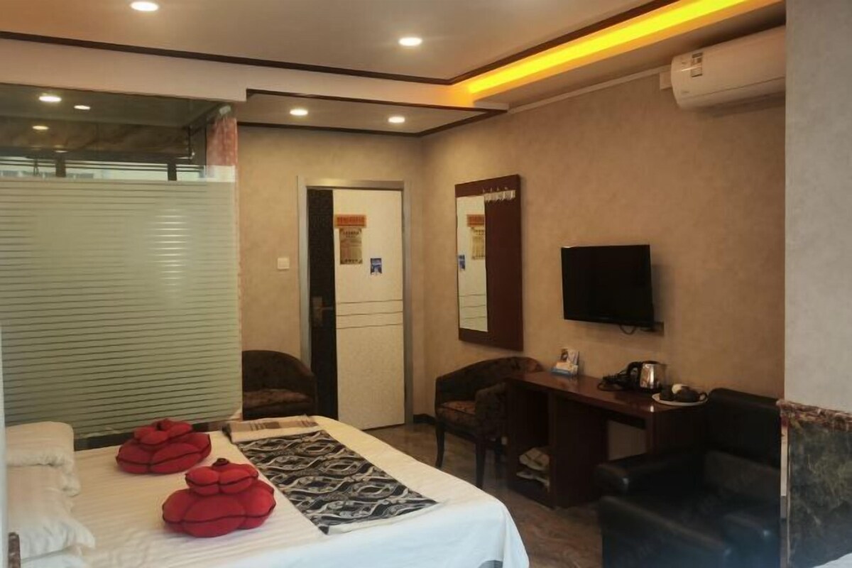 A hotel room with a bed, a desk, a chair, a television, and a mirror.