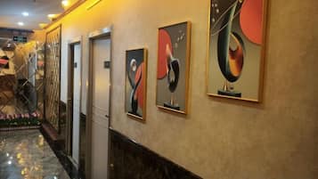 A hallway with artwork on the walls, a marble floor, and a door on the left.