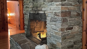 A stone fireplace with a metal screen, a white stone on the hearth, and wooden flooring.