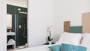 A modern bedroom with a bed, white pillows, a nightstand, a potted orchid, and a glass-enclosed shower area. - Nimar suite (Formia)
