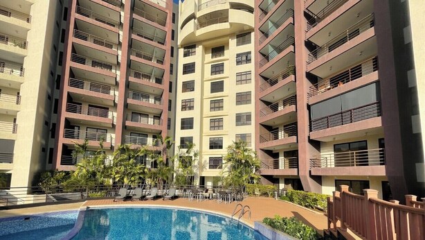 A modern apartment building with a swimming pool, balconies, and palm trees.