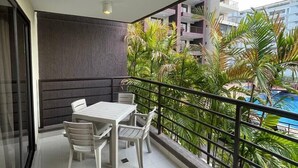 A balcony with a table and chairs, a view of a swimming pool, and a cityscape in the background.