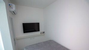 A small, sparsely furnished room with a bed, a mounted television, and an air conditioning unit. - KITNET in the heart of Salvador/BA: Barra (Barra Salvador)