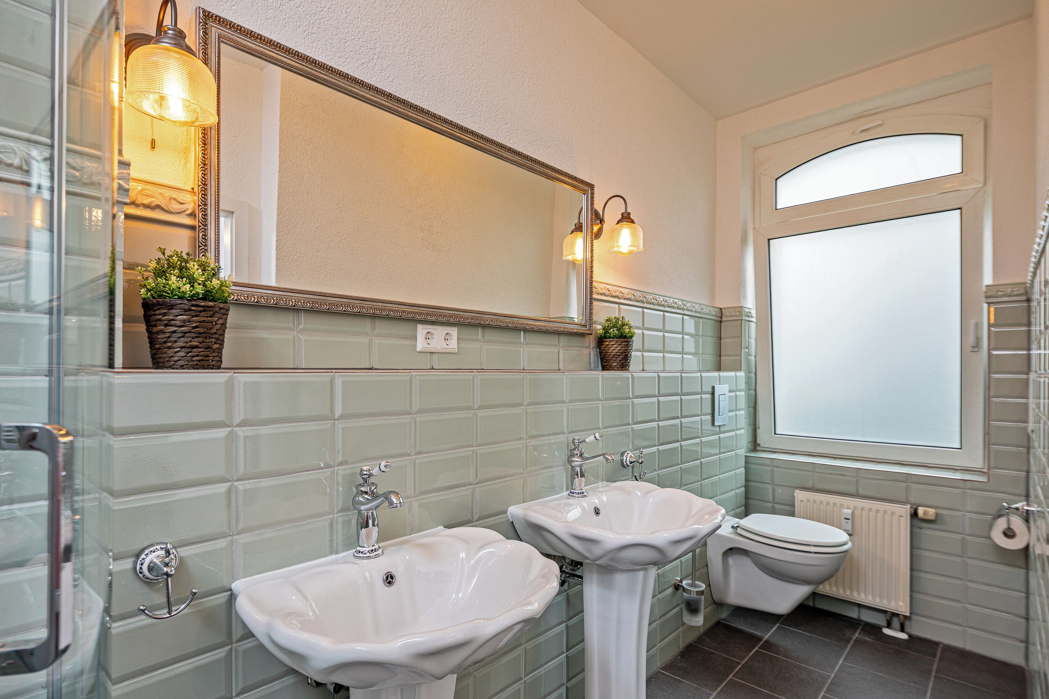 Un baño con dos lavamanos, un inodoro, un espejo grande y una ventana.