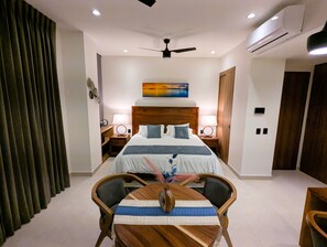 A modern hotel room with a large bed, a ceiling fan, an air conditioning unit, a painting on the wall, and a dining table with chairs. - Condo Marsala 603 Studio, Close To The Beach, Rooftop, Great Views, heated pool (Bucerías)