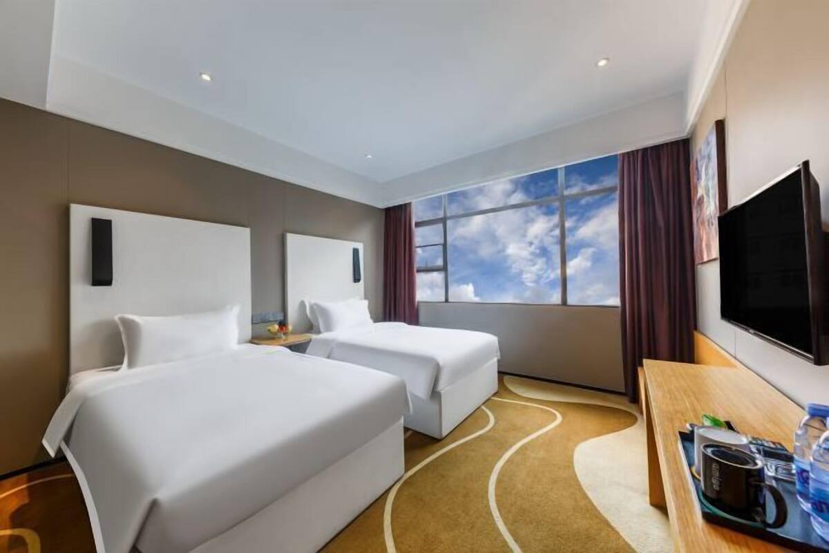 Une chambre d’hôtel avec deux lits, une grande fenêtre donnant sur un beau paysage, un téléviseur à écran plat et un bureau équipé d’une machine à café.