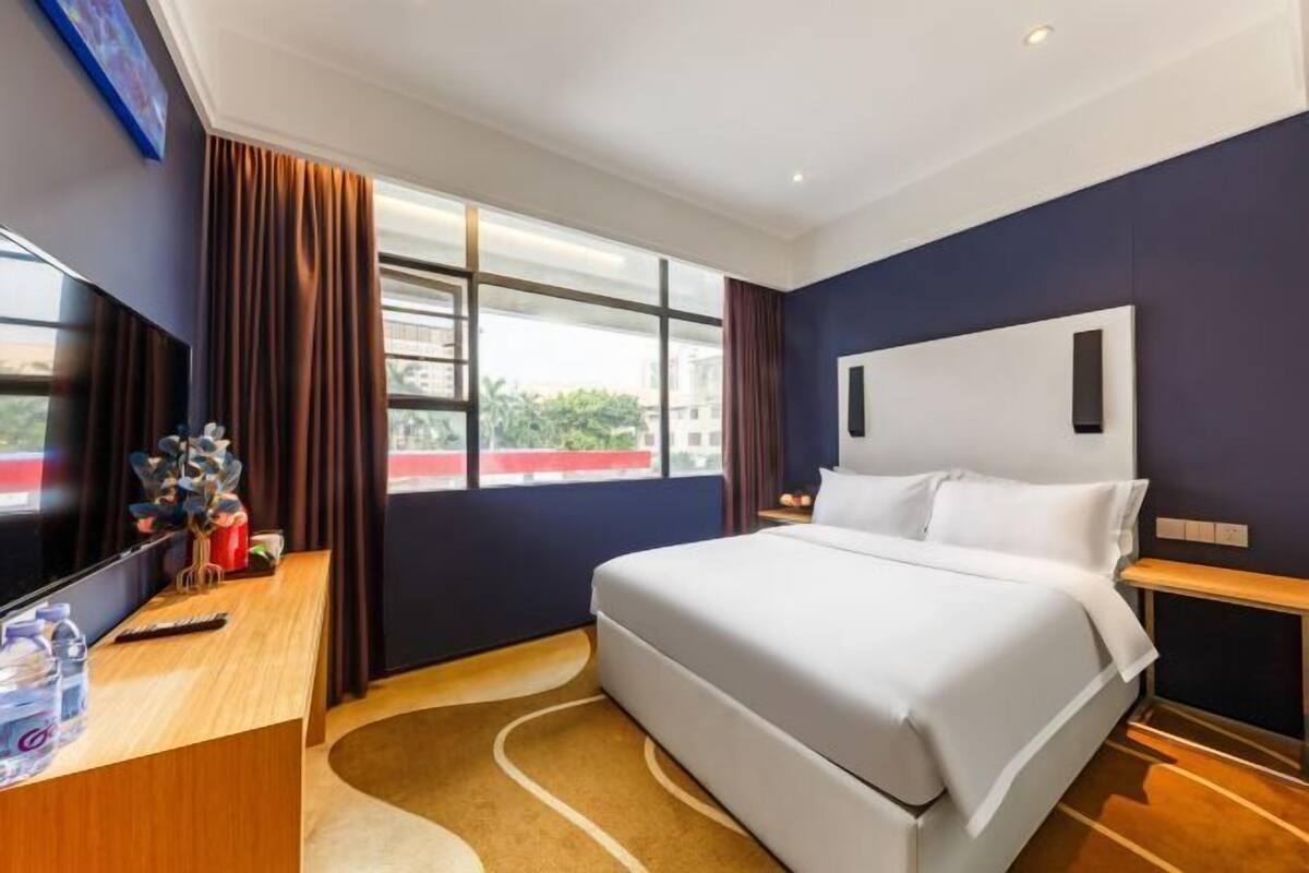 Une chambre d’hôtel avec un lit, un bureau, une télévision et une fenêtre avec des rideaux.