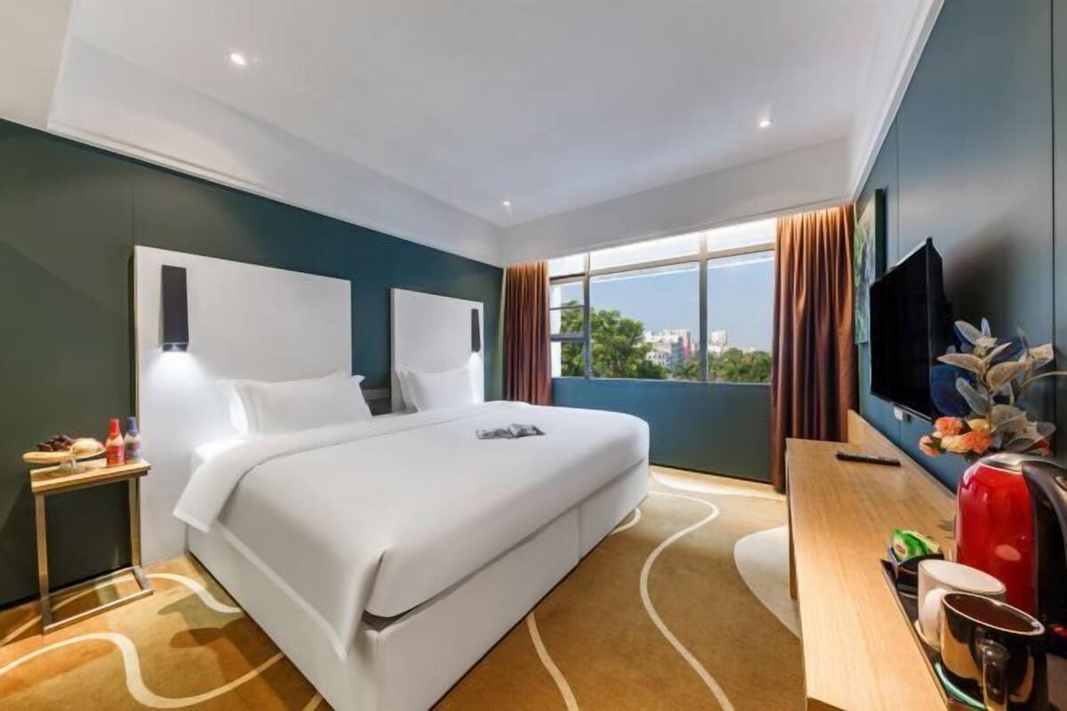 Une chambre d’hôtel équipée d’un lit, d’une télévision, d’un bureau avec une machine à café et d’une fenêtre avec des rideaux.