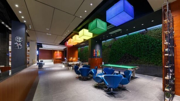 Un espacio interior moderno con mesa de billar, sillas azules y una pared verde con plantas.