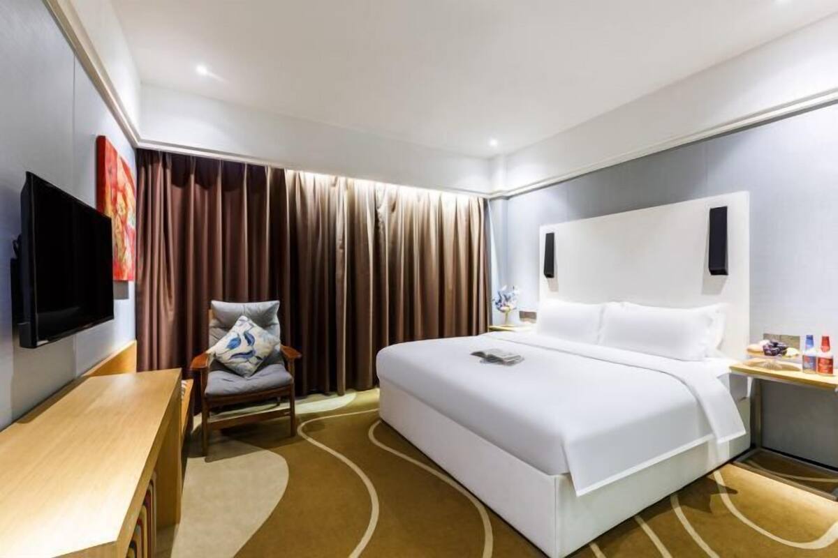 Une chambre d’hôtel avec un lit, une télévision, une chaise, un bureau et une fenêtre avec des rideaux.