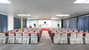 Un salón de conferencias con varias mesas y sillas, un atril y una pantalla que muestra el logotipo 'AMIGO'.