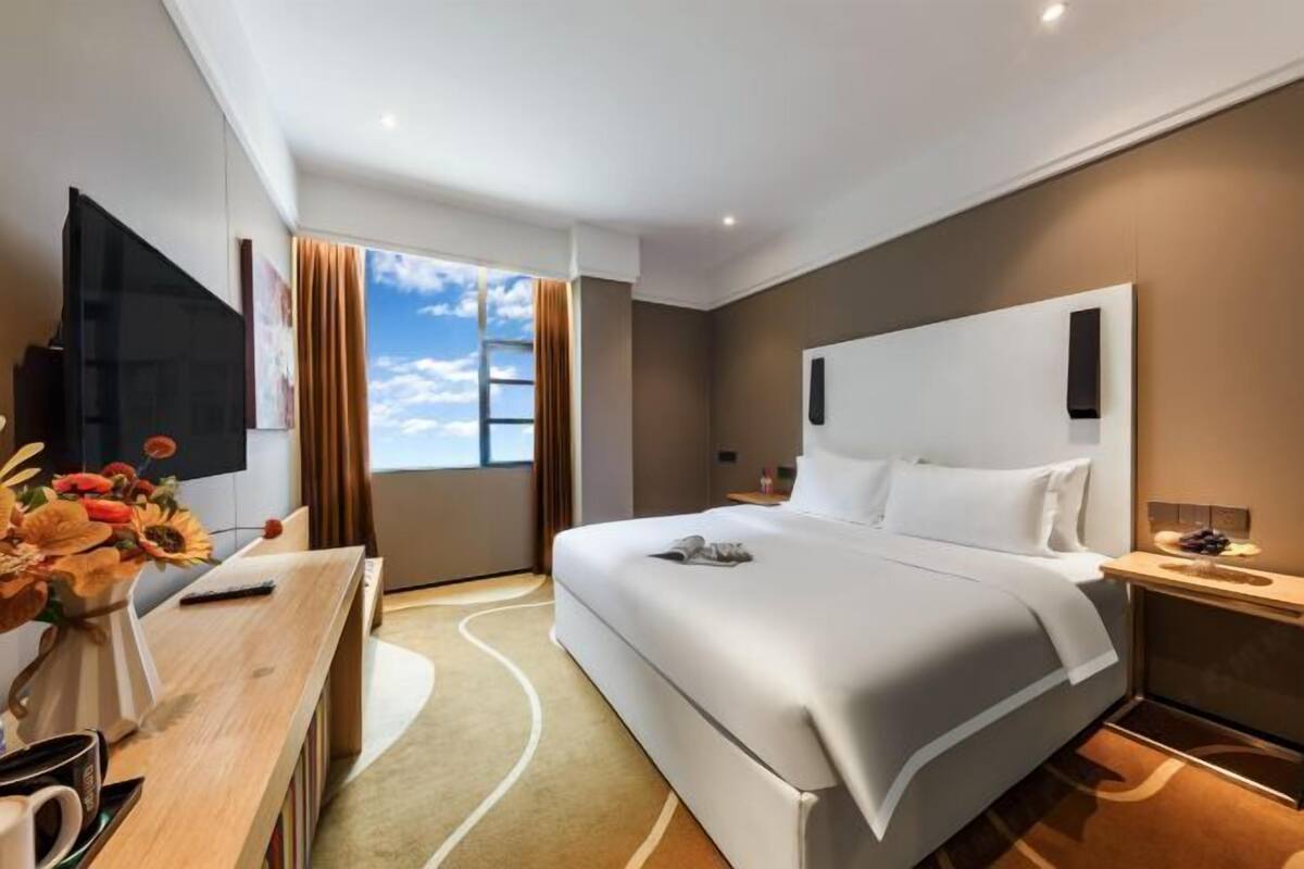 Une chambre d’hôtel moderne dotée d’un grand lit, d’un bureau avec un téléviseur à écran plat, d’une fenêtre avec des rideaux et offrant une vue sur le ciel.