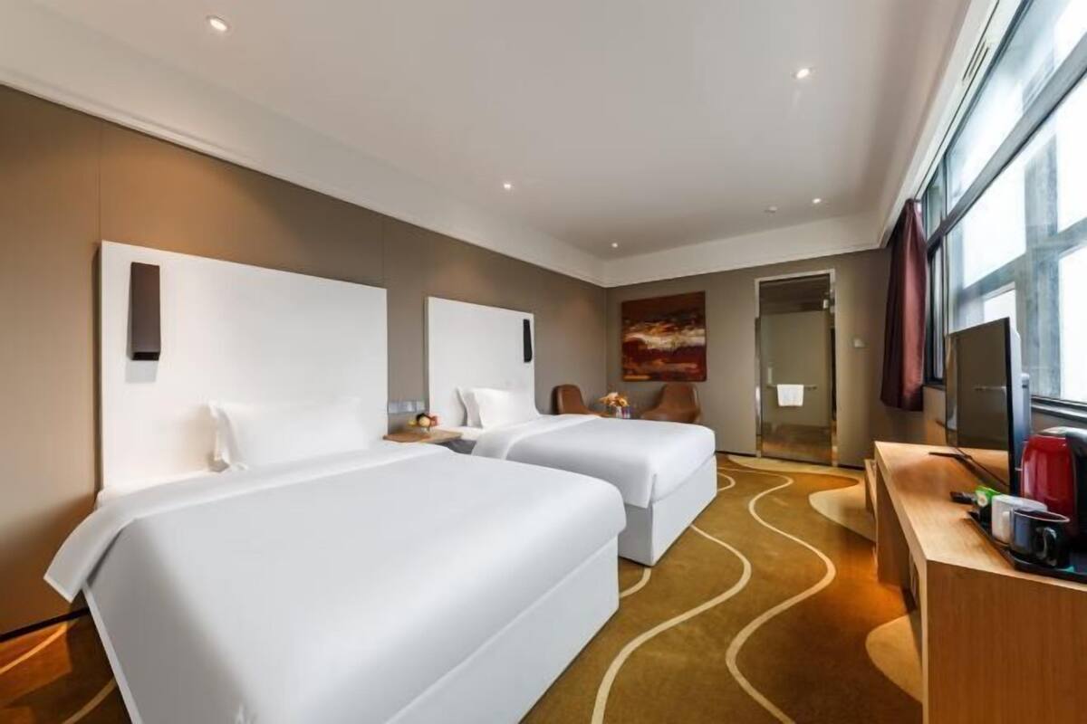 Une chambre d’hôtel avec deux lits, un bureau, une chaise, une télévision et un tableau au mur.