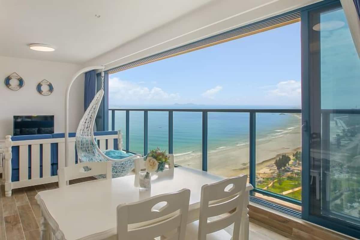 A balcony with a view of the beach, a white dining table, and a TV.