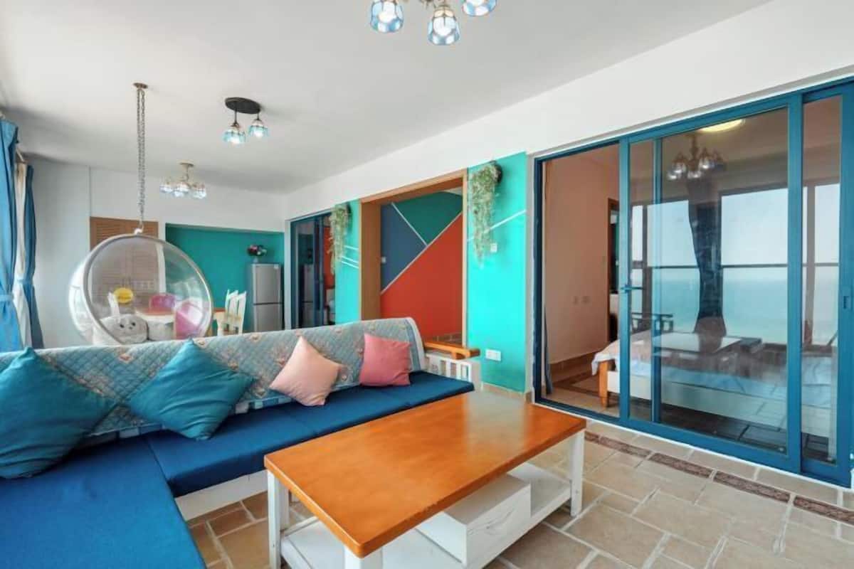 A modern living room with a sofa, a coffee table, and a glass door leading to a balcony.