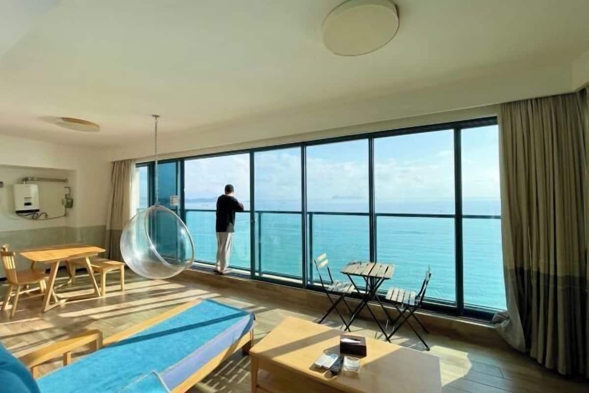 A hotel room with a large window, a view of the sea, a hanging chair, and a pool table.