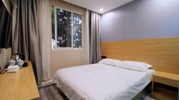 Habitación de hotel con cama, mesita de noche de madera, escritorio con silla y ventana con cortinas.