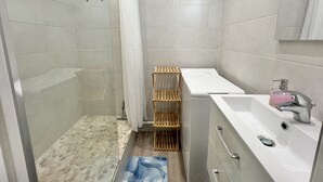 Ein modernes Badezimmer mit Dusche, einer integrierten Waschmaschine und einem Waschbecken mit Armatur.