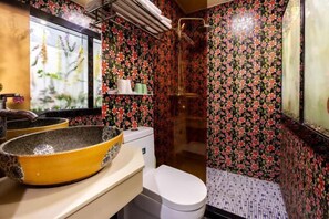 Ein Badezimmer mit floralem Wandpapier, einem gelben Waschbecken, einer weißen Toilette und einem Duschbereich.