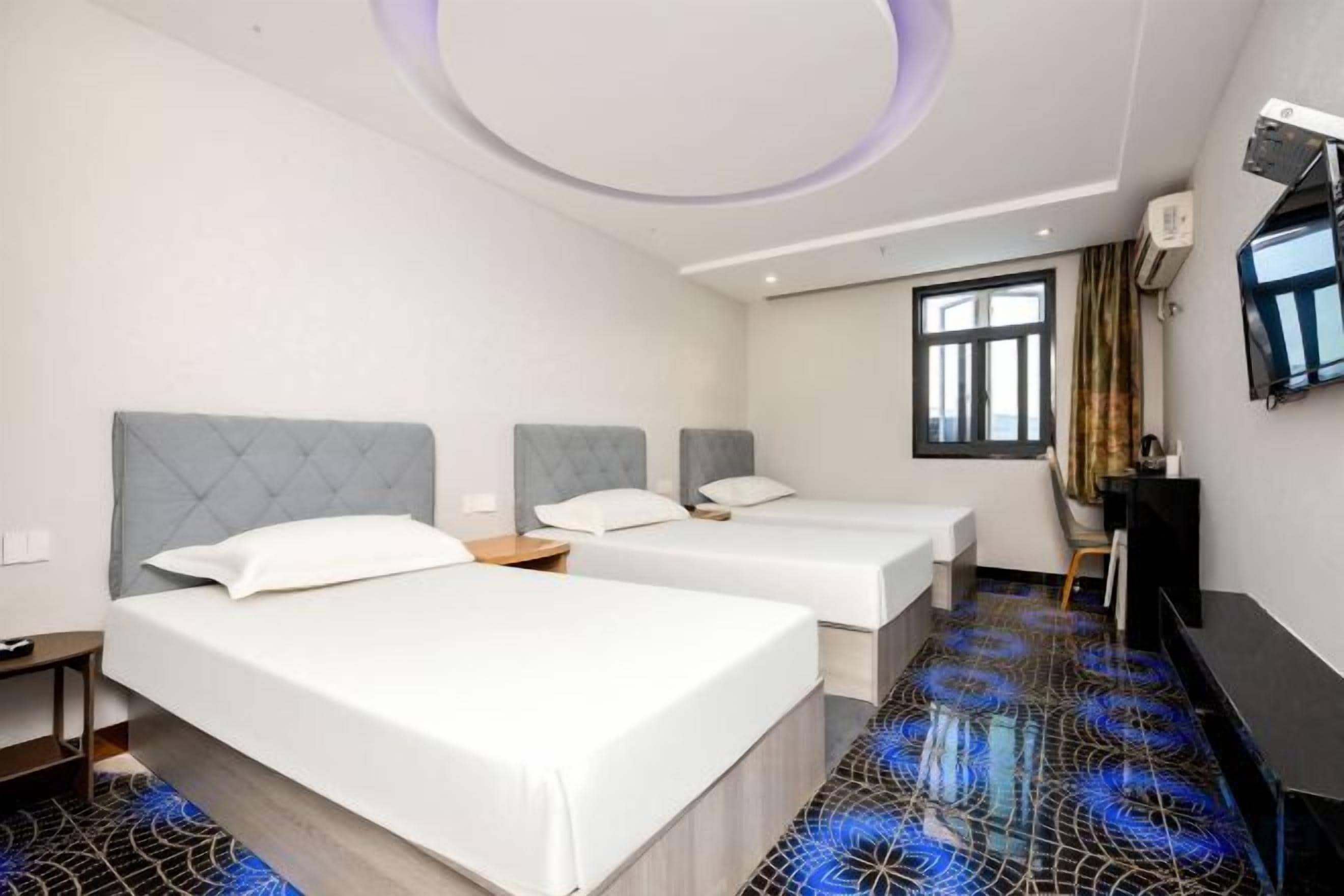 A hotel room with two beds, a flat-screen TV, and a patterned floor.