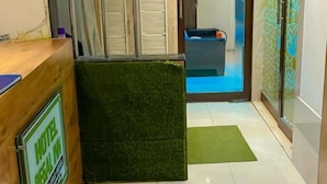 A hotel reception area with a reception desk, a clock, and a view of the pool area. - New Regal By Glitz Hotels (Mumbai)