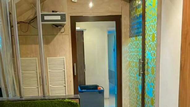 A hallway with a green artificial grass area, a blue sofa in the background, and a patterned door. - New Regal By Glitz Hotels (Mumbai)