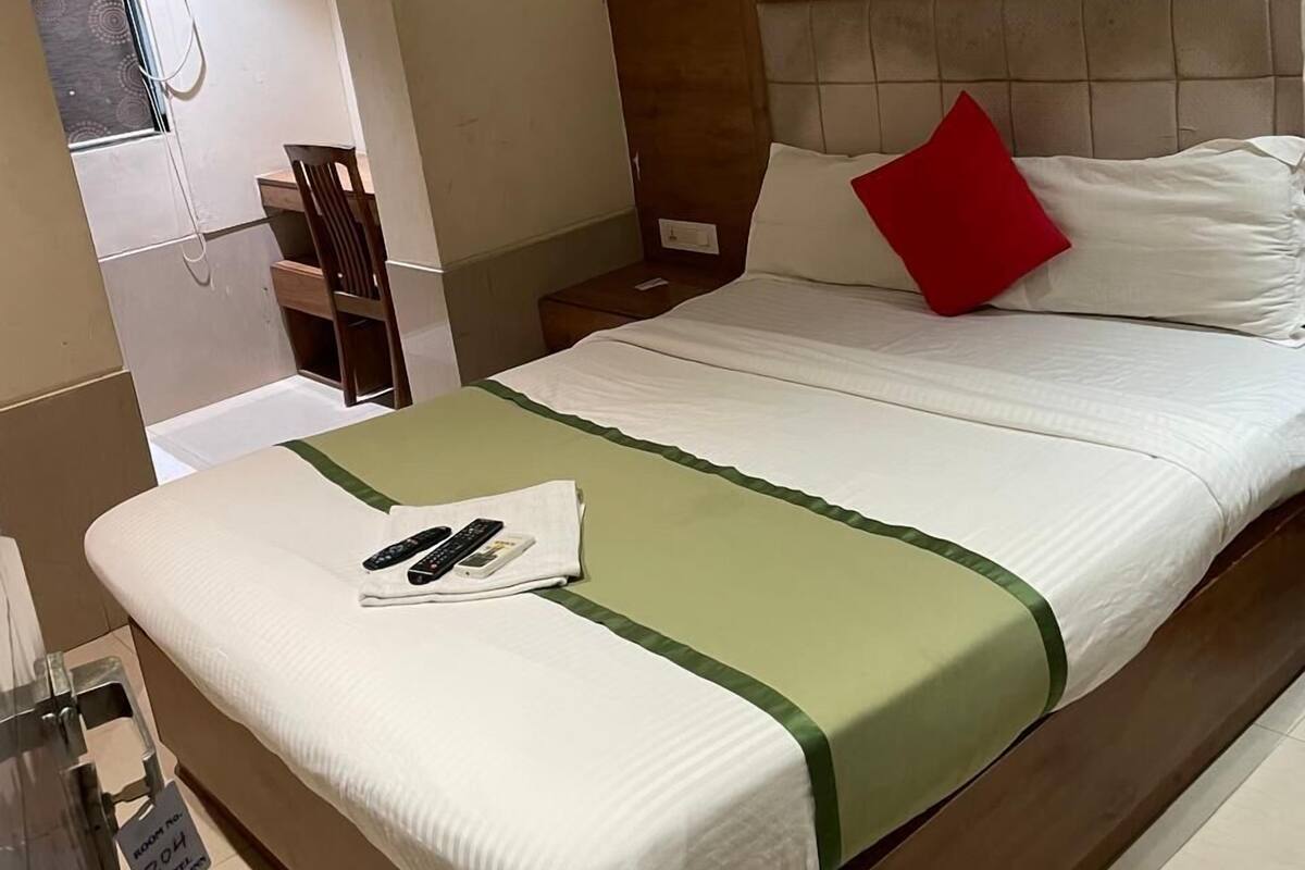 A hotel room with a bed, a nightstand, a chair, a window with a shower, and a sign indicating the room number.