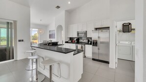 A modern kitchen with white cabinetry, stainless steel appliances, and a central island with bar stools. - EV_149 - 5 Bed 3 Bath Home with Private Screened-In Pool, Games Room (Davenport)