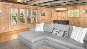 Una stanza accogliente con un divano angolare grigio, pareti in legno, ampie finestre e una ventola a soffitto.