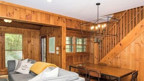 Interno di una baita in legno con divano, tavolo da pranzo e scala.