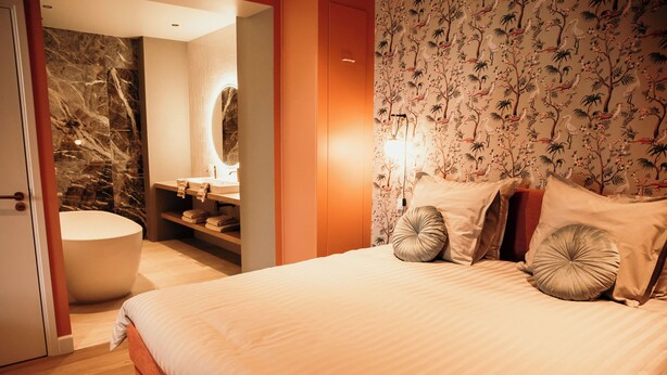 A bedroom with a large bed, a bathroom with a marble wall, and a floral wallpaper design.