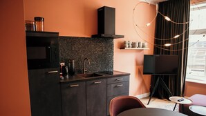 A modern kitchen with a microwave, sink, and black cabinets. There is a television and a small table with a chair.