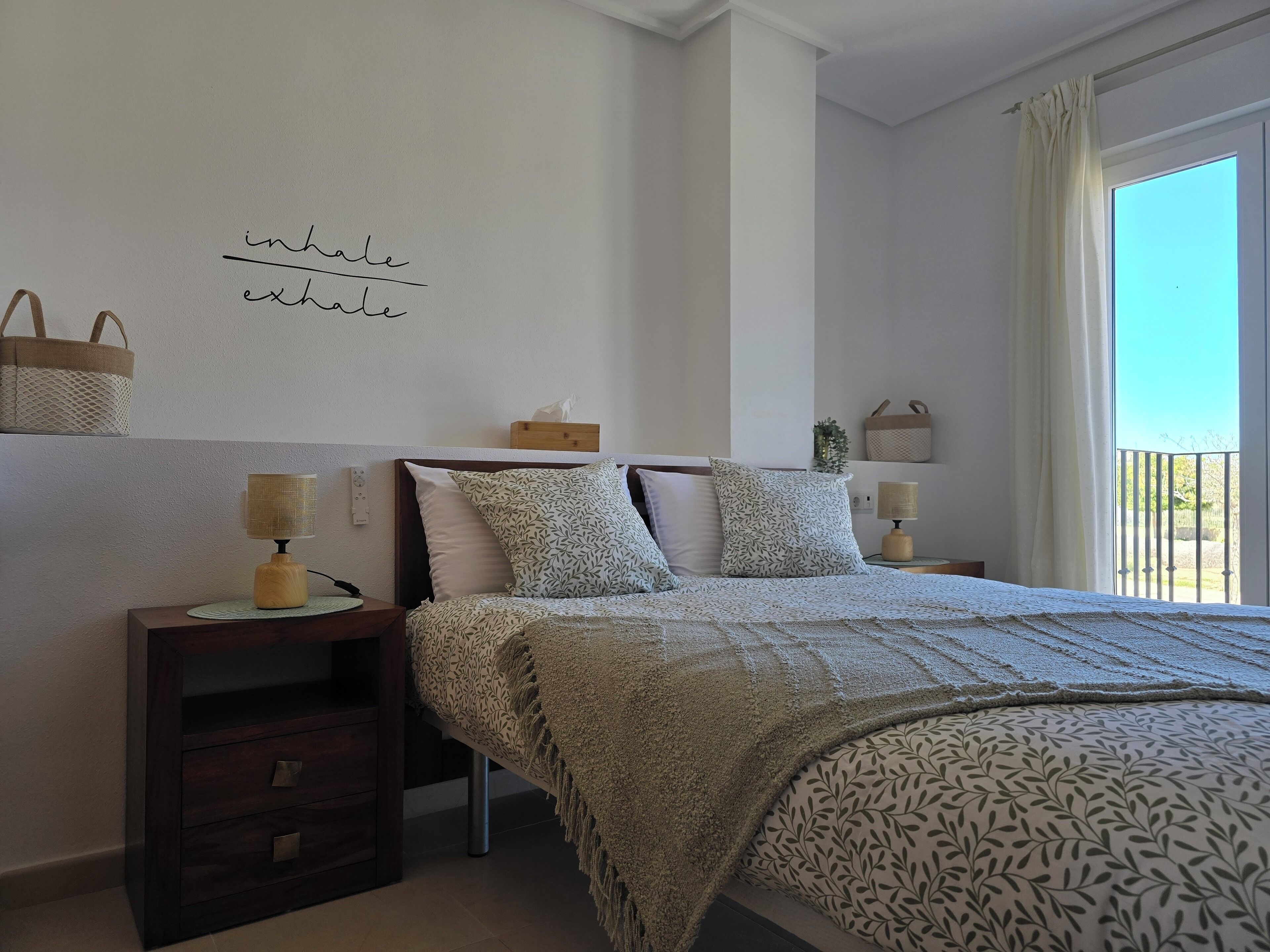 A bedroom with a bed, bedside tables, a wall-mounted shelf with baskets, and a window with curtains.