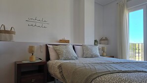 Un dormitorio con cama, mesitas de noche, un estante en la pared con cestas y una ventana con cortinas.